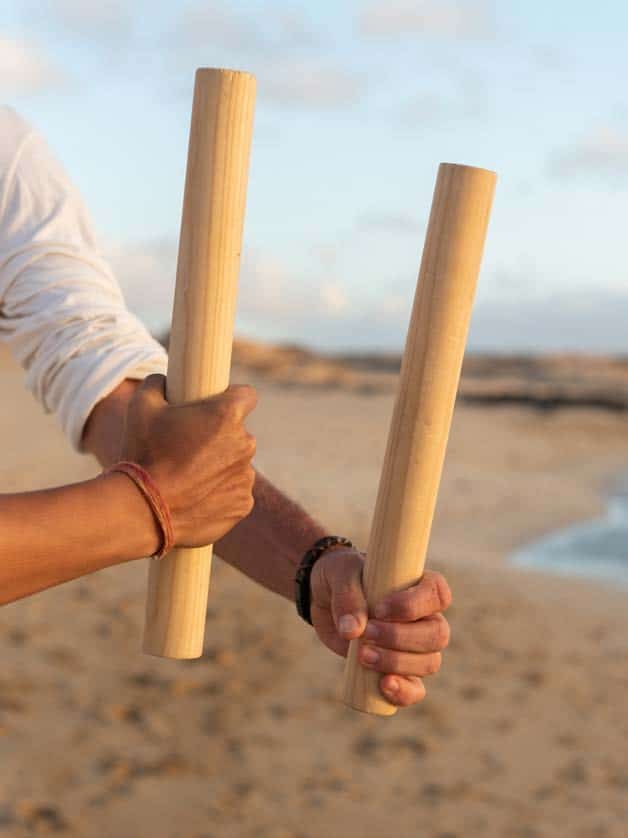 Nuanu-Co-Creation Hände die zwei Bambusstöcke in der Hand halten am Strand