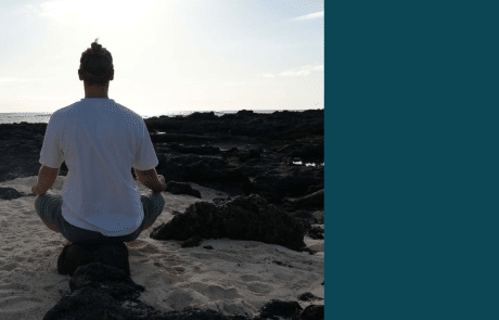 Mann im Schneidersitz mit Meer im Hintergrund